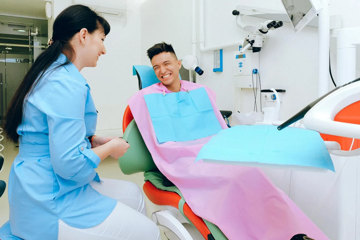 Happy ethnic guy sitting in dental chair and smiling while talking with female dentist in uniform before treatment in modern clinic
