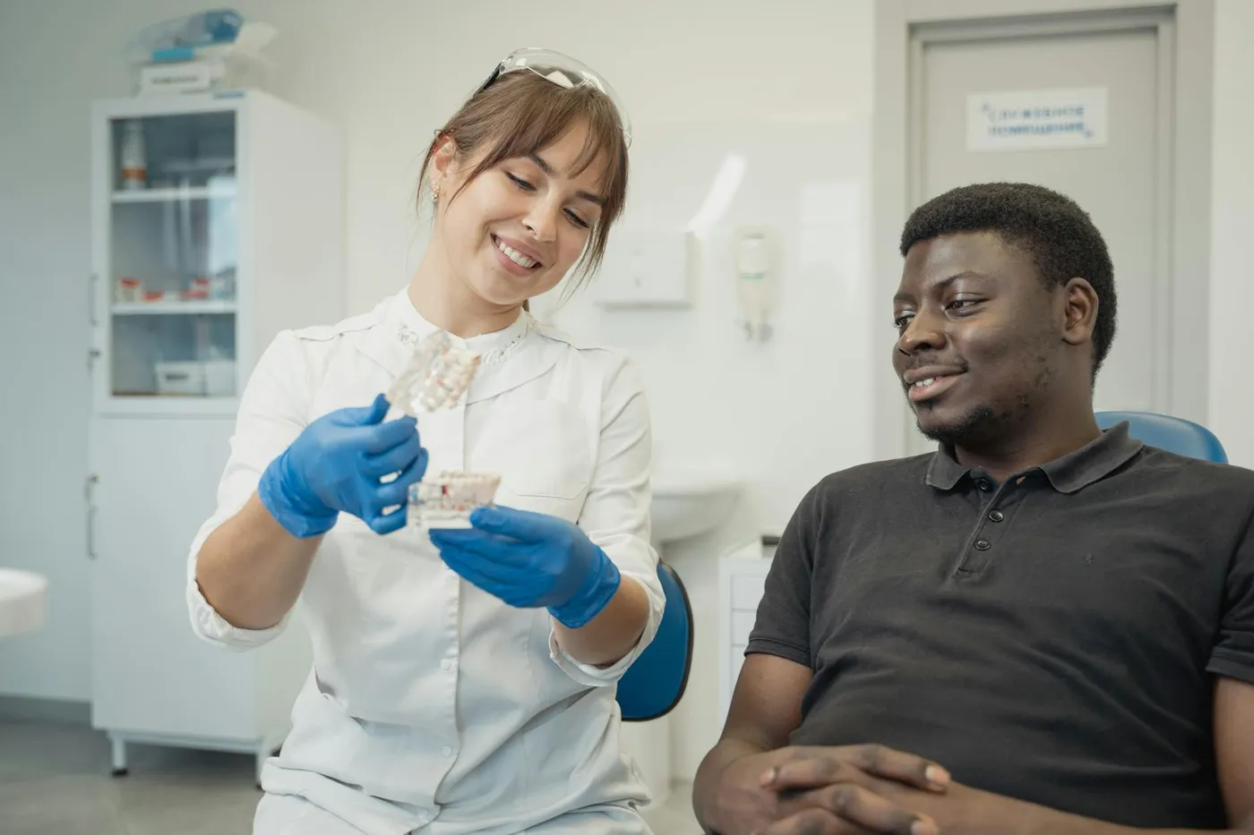 Smiling dentist shows dental model to relaxed patient during consultation at clinic.