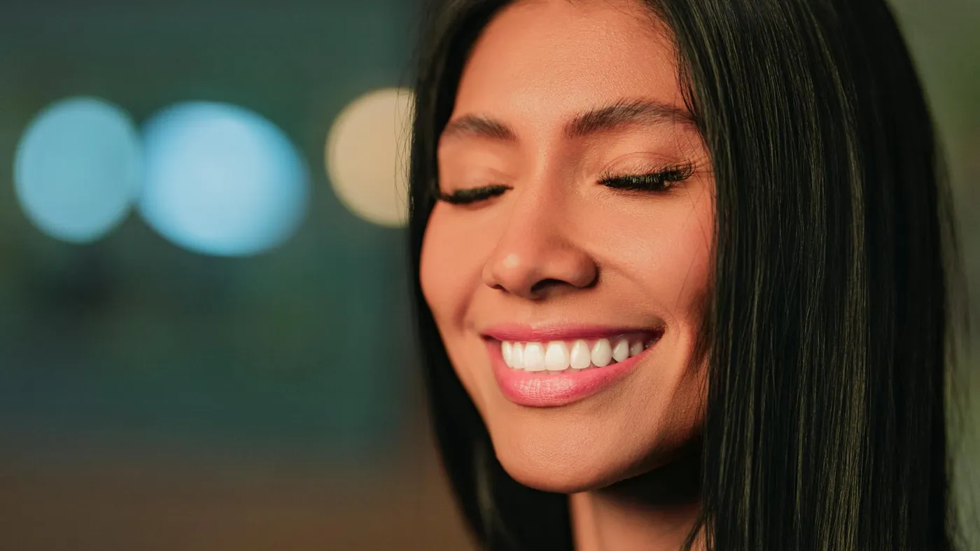 Close-up portrait of a woman smiling with eyes closed, in soft focus lighting.