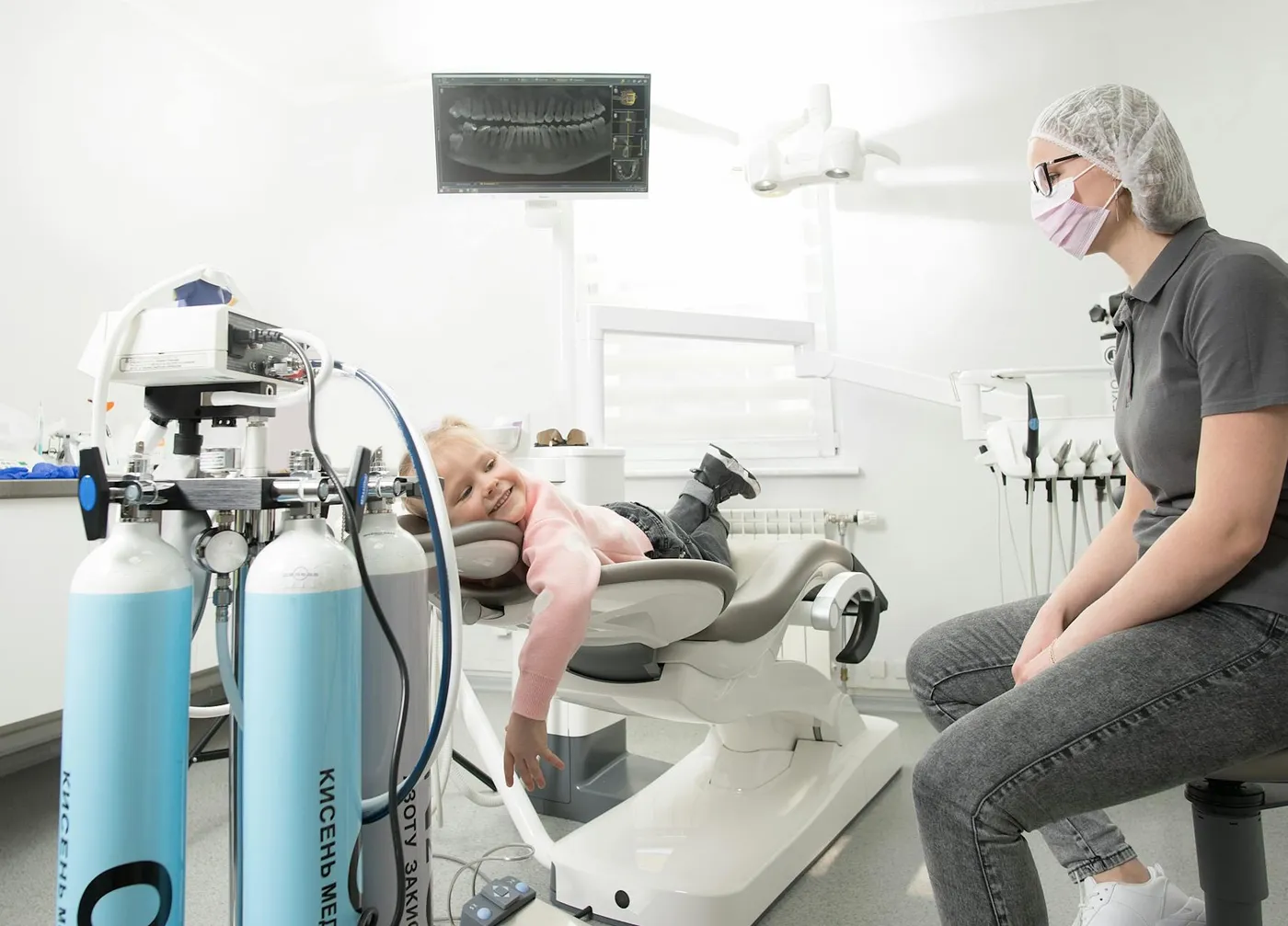 A child with a bright smile during a dental check-up in a Kyiv clinic. Friendly healthcare professional nearby.